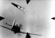 Gunsight view: In the bottom left, a fighter aircraft is seen from the rear, its tail plane is separated and above it, a cluster of bright tracer can be seen picture center-right.