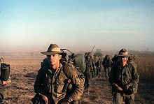 A group of men wearing green military uniforms walking across barren ground.