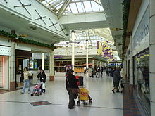 Shopping mall thoroughfare with two storey glazed roof and white marble flooring lined on either side by rows of shops