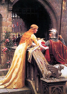 A young woman in a medieval-style dress of cream satin ties a red scarf to the arm of a man in armour and mounted on a horse. The scene is set at the portal of a castle.