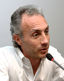 40-ish man with grey hairs, talking on a microphone.