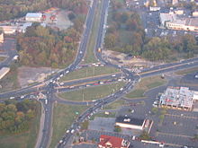 An aerial view of an intersection between two roads, with the top to bottom road splitting into a circular intersection and the left to right road running straight through