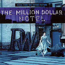 A blue-tinted photograph of a Caucasian woman in her 30's—Milla Jovovich—running barefoot across the rooftop of a brick building wearing a long dress. Above her are the captions "MUSIC FROM THE MOTION PICTURE" written in blue on black and "THE MILLION DOLLAR / HOTEL" written with light bulbs.