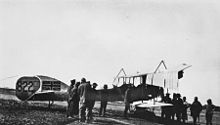 A group of men gather around a biplane. The Union Jack has been painted on to the tail of the aircraft