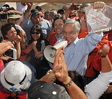 Color image of President Piñera displaying the message in a plastic document protector sent by the miners with Mining Minister Golborne