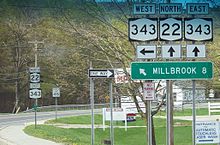 A sign assembly indicates that NY 343 westbound is accessed by turning left while NY 22 northbound and NY 343 eastbound are straight ahead. A sign below the route shields indicates that Millbrook is located eight miles to the west on NY 343.