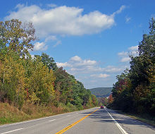 A straight two-lane road with trees on either side leading off into the distance toward a ridge