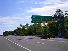 Overhead sign on a four-lane road with a New York state route marker instead of the pentagonal county shield