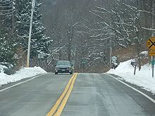 A road in a forested area. The surrounded land is covered with a layer of snow.