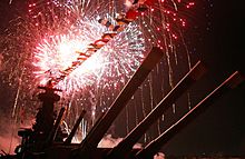 Red and yellow fireworks fill the sky, as seen from the deck of the ship. The main guns loom directly overhead.