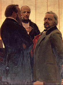 Three men standing together - two men with beards, the one on the right with grey hair, flanking a third man watching them intently