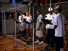 A woman and four men recording a song in a studio.