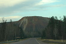 A roadway leading away into the distance before curving in front of a large pile of waste rock