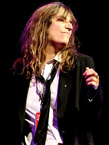 A photograph of Patti Smith looking to the side of the camera while performing onstage