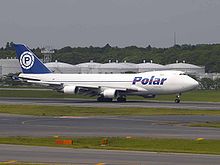 A white four-engine jumbo jet with a blue Polar logo, rolling out on an airport runway.