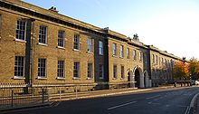  A long, two storied building with a flat roof, large Georgian windows and a three arched gateway