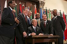 Rangel and six other men stand around a table, where President George W. Bush signs a bill
