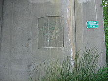 A concrete bridge support with State Highway Route 42 stamped onto it. A green sign seen to the right on the bridge support reads 0114-155 34.69