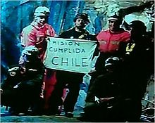 Slightly grainy color video capture image of the six rescuers displaying the famous "Mision Cumplida Chile" sign deep within San José Mine near Copiapo, Chile [125]