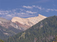 A light brown, almost white mountain rises above forested hills