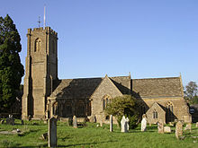Stone building with square tower to the left hand end. In the foreground are gravestones.