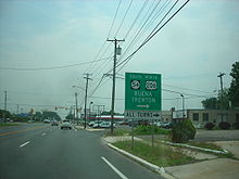 A four lane undivided road in a business area approaching a traffic light. A sign on the right side of the road reads south Route 54 north U.S. Route 206 Buena Trenton right all turns right