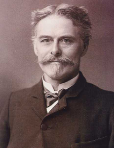 Head and shoulders of a middle-aged man who is looking at the viewer. He has a moustache and goatee, and his hair is short and parted in the middle. He is wearing a formal jacket, with a bow tie and wingless collar.