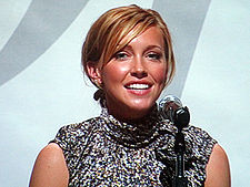 A smiling, blond woman in front of a microphone.