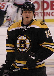Caucasian male wearing black helmet, black jersey with a spoked B located in the middle. He is holding a hockey stick.