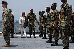 A colour photograph of soldiers on a naval vessel being inspected by President Ellen Johnson Sirlef and a senior military officer. The soldiers are wearing disruptive pattern camouflage uniforms and are standing in ranks across the deck