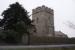 Square stone tower, behind a stone wall and partially obscured by a tree.