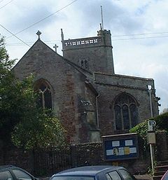 Red and grey stone building with arched windows and triangular roof. Behind is a small square tower