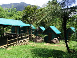 Several bungalows made of wood and blue-green tarp, along with a covered eating area.
