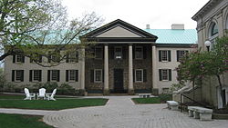 A stone and cream colored building with a green roof and a large portico