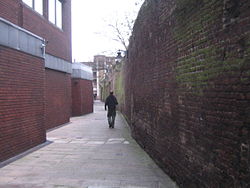 A view down an alleyway, bounded by a red brick wall on the right, and red brick buildings on the left.