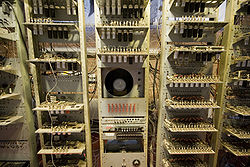 Close-up view of three tall racks containing electronic circuit boards, with a cathode ray tube in the middle of the central rack. Below the CRT is a panel containing four rows of eight switches.