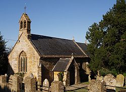 Stone building with arched window and slate roof. In the foreground are gravestones