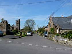 Street scene showing houses on the left and church with square tower on the left.