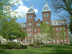 A red brick building with a mansard roof and two identical towers at the top surrounded by trees