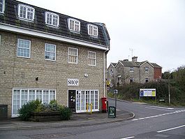 Stone 3 storey building with white frames windows on street junction. Sign saying shop.