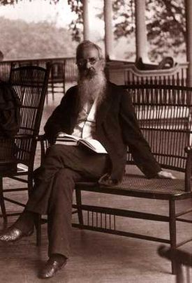 an elderly man with a long beard is seated on a veranda