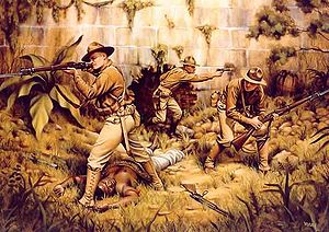 A painting of three Marines fighting in a jungle. There is a brick wall in the background with a lot of plants and trees. An enemy fighter is in the foreground and appears to be dead.