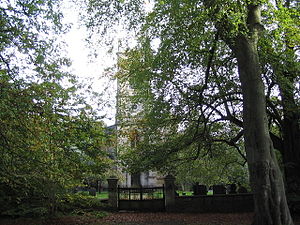 Almost obscured by trees is the tower of a stone church beyond a gate