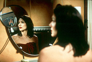 Laura Elena Harring wet from a shower and wrapped in a red towel, looking into the mirror at a reflection of the theatrical poster for the film Gilda