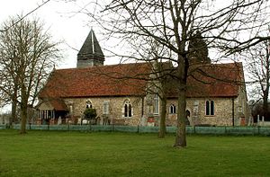 alt=A stone church with red tiled roofs seen from the south, showing the chancel, the south aisle and porch, and the tower with a pyramidal roof