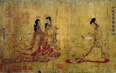 Two ladies walking towards another lady standing at a writing table with a writing brush in her hand